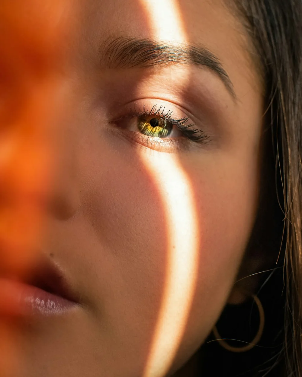 Retrato em close de uma mulher com feixe de luz dourada no rosto e argola